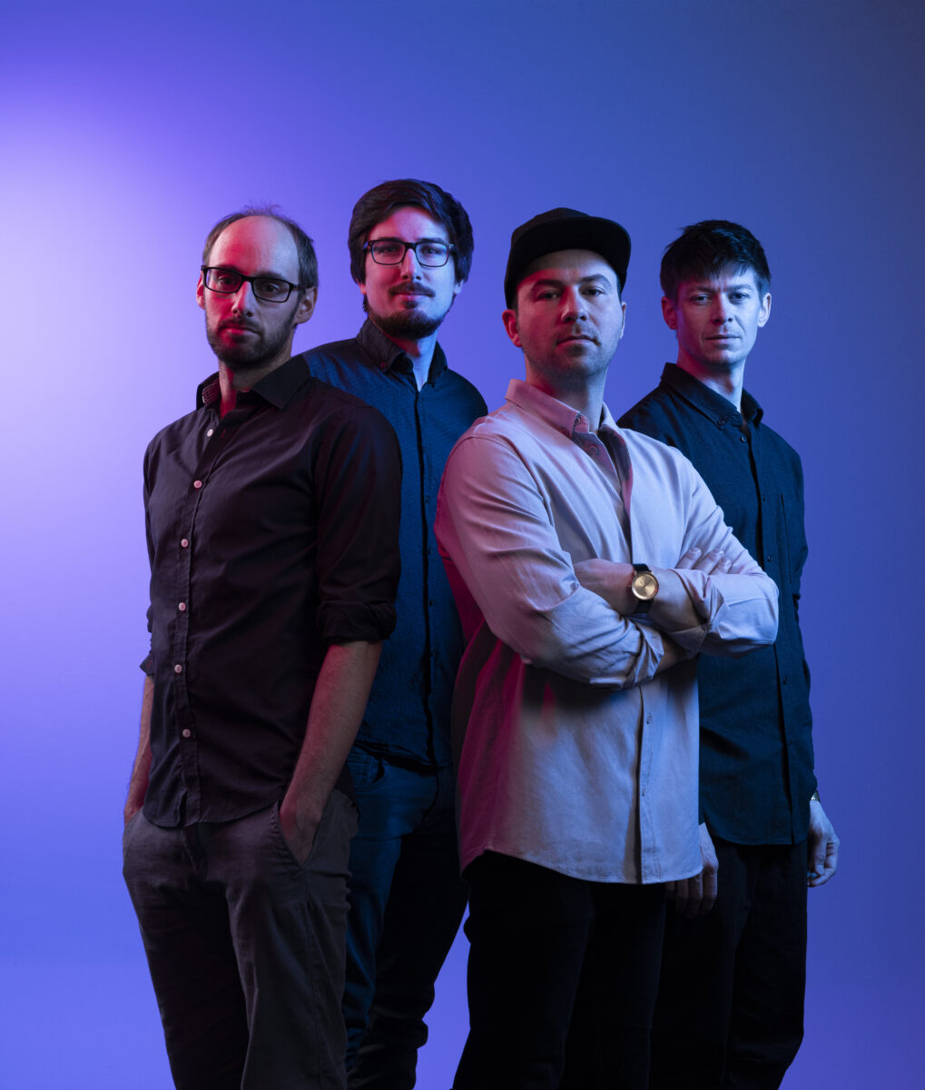 four young men dressed in dark shirts in front of blue background