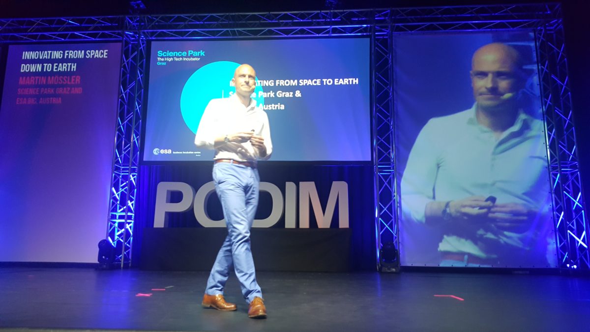 Key note speaker Martin Mössler on stage and on a screen, next to a displayed presentation and podim logo