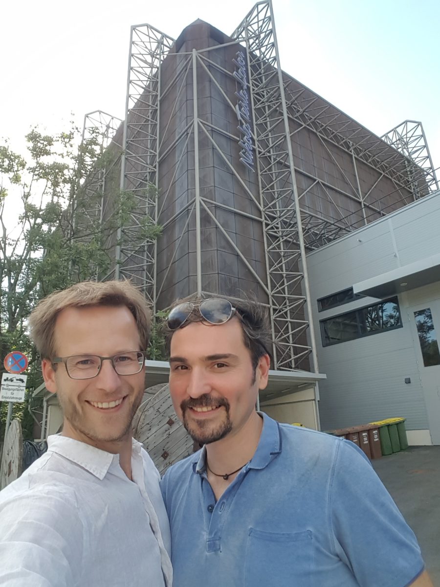 Two men, founders, standing in front of a house