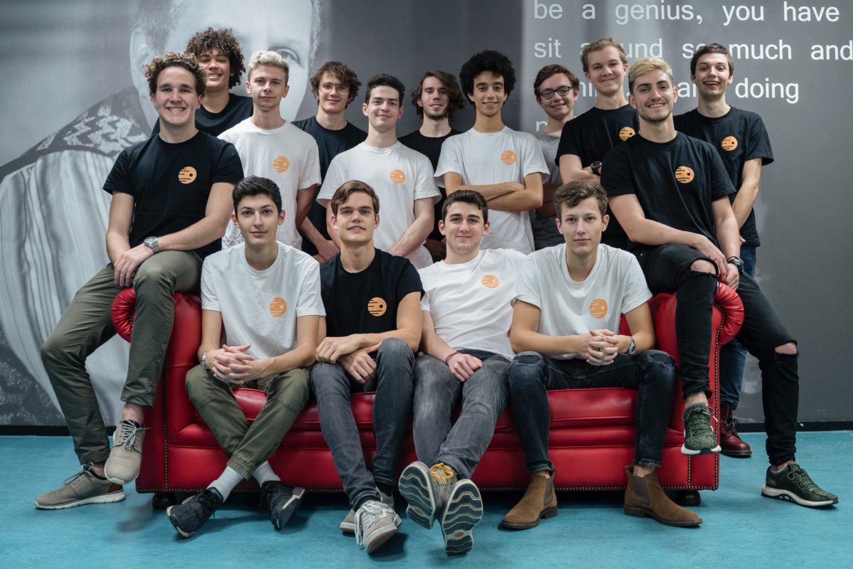 team of 25 young men, 4 sitting and 11 standing behind a red sofa