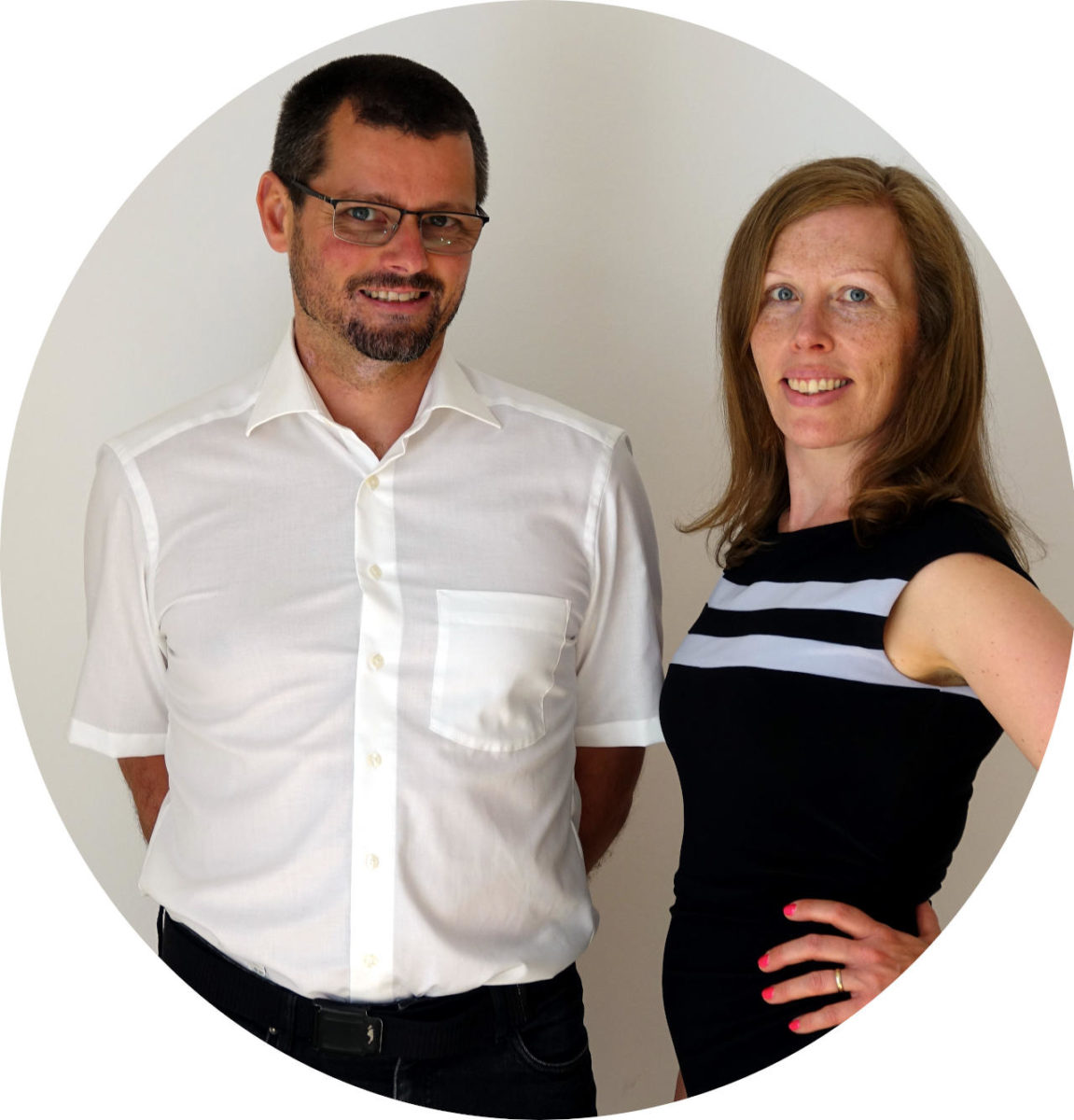 Founders, man with glasses and white shirt and woman with red hair in a dress, standing in front of grey background