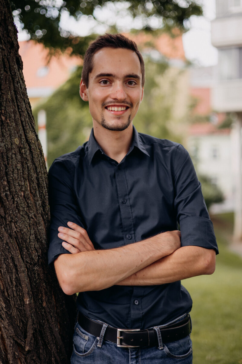 Young man in dark shirt leaning on a tree