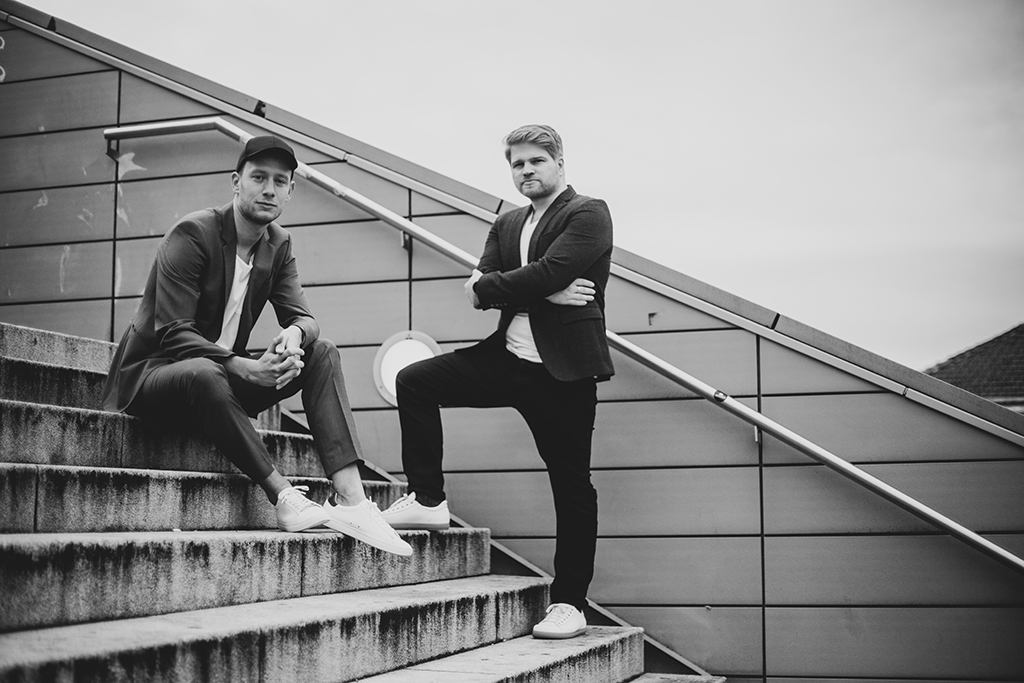 Black and white photo of two men,one sitting, one standing, on a staircase